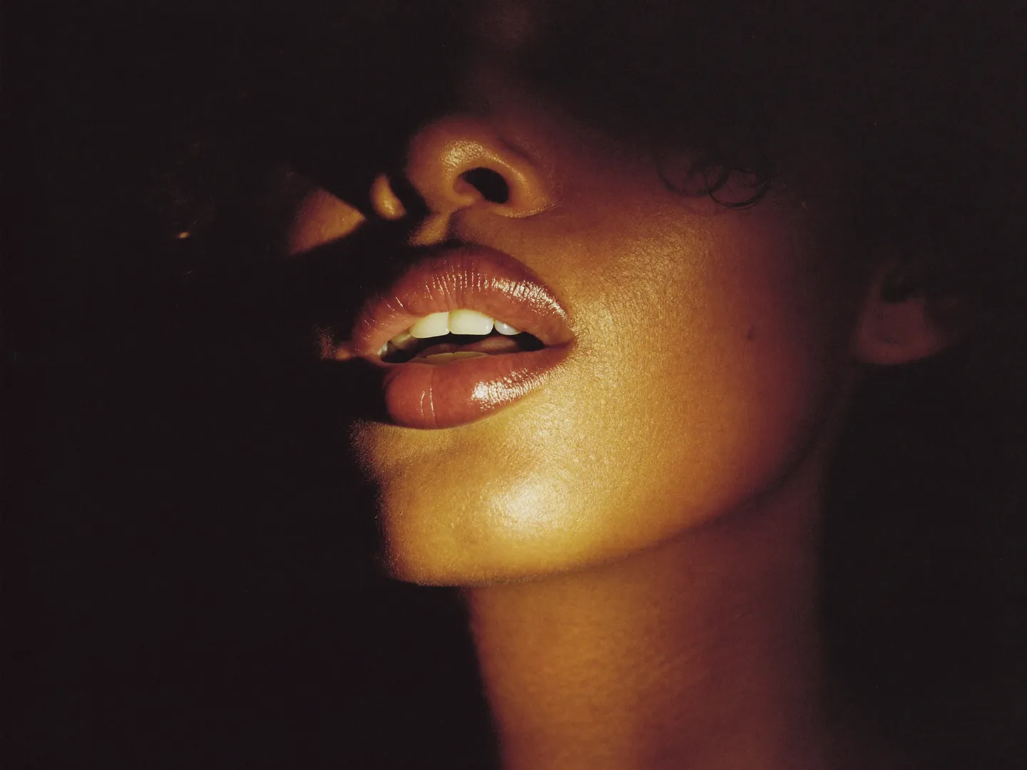 A close-up of a woman's glossy lips, parted, in low warm light