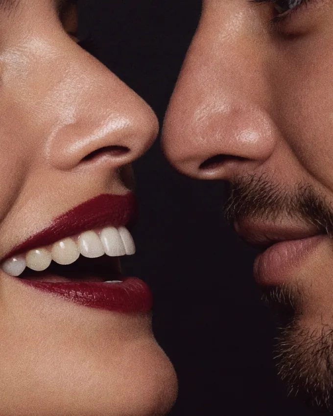 A woman with red lips smiling, her face close to a bearded man's, their mouths almost touching